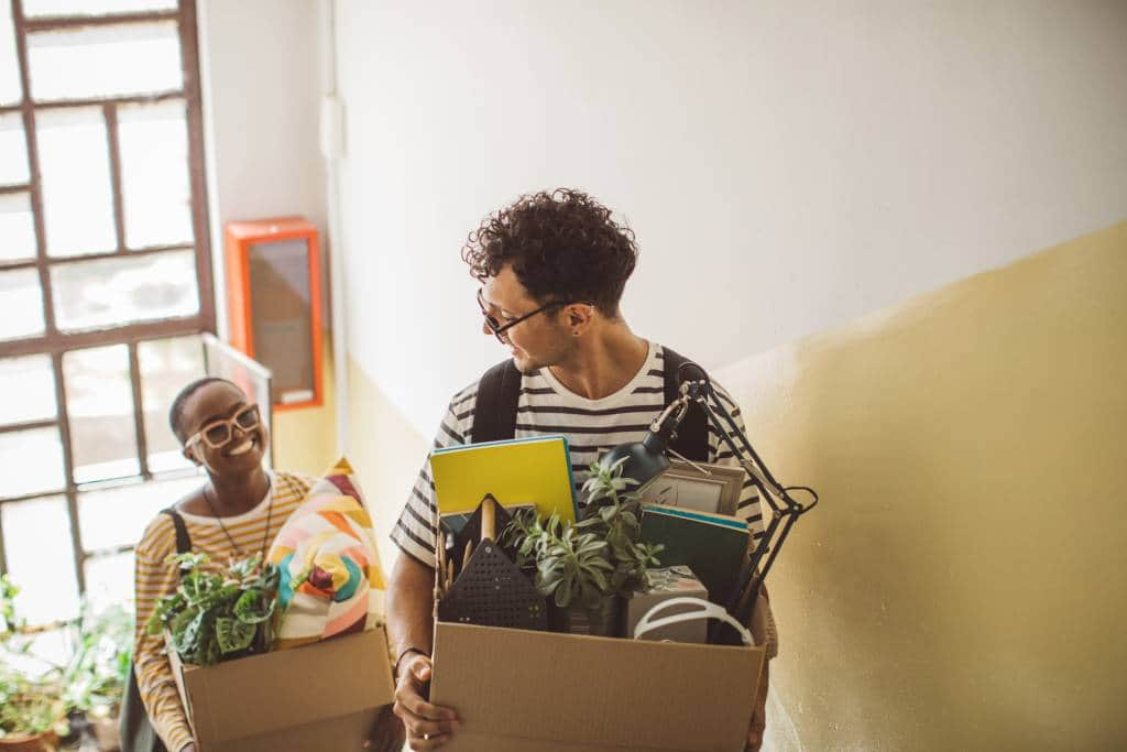 students carrying boxes of plants and knick-knacks as they move into a dorm