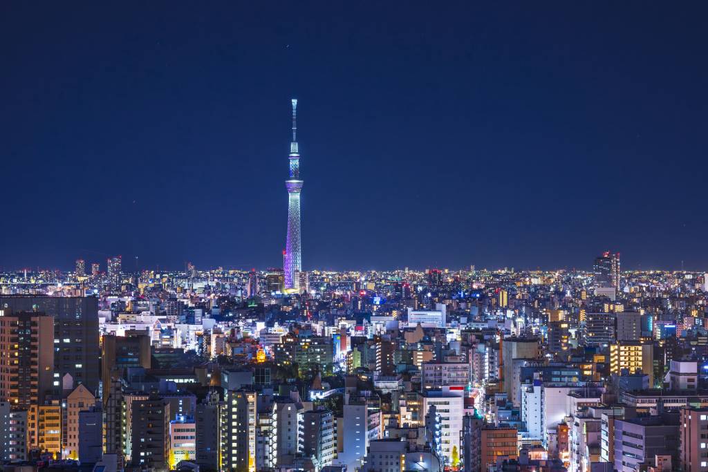 Tall skinny steel tower illuminated purple and blue against an evening sky