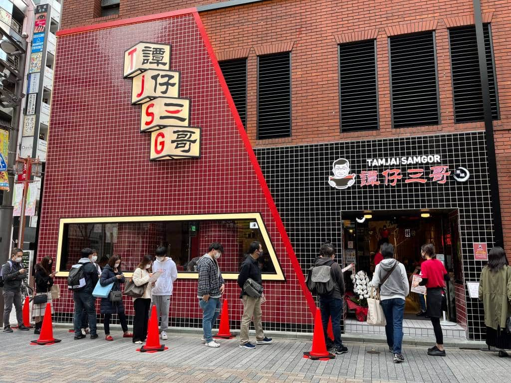 Queue of people outside noodle store with black and red tiles