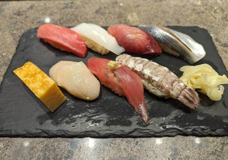 Different types of nigiri sushi sit on a black stone plate.