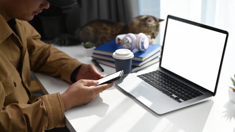 a man uses his wifi-connected cell phone and laptop at home, with a cat in the background